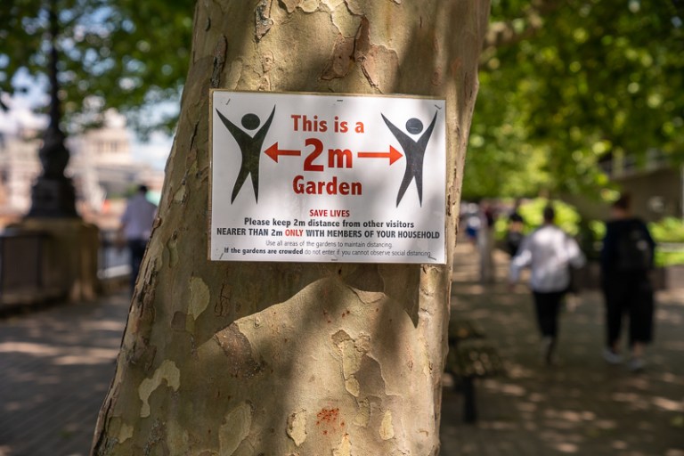 Sign on tree warning about social distancing and people in the background