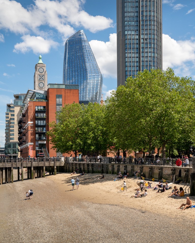 People lying on the beach of the Thames with Oxo Tower behind