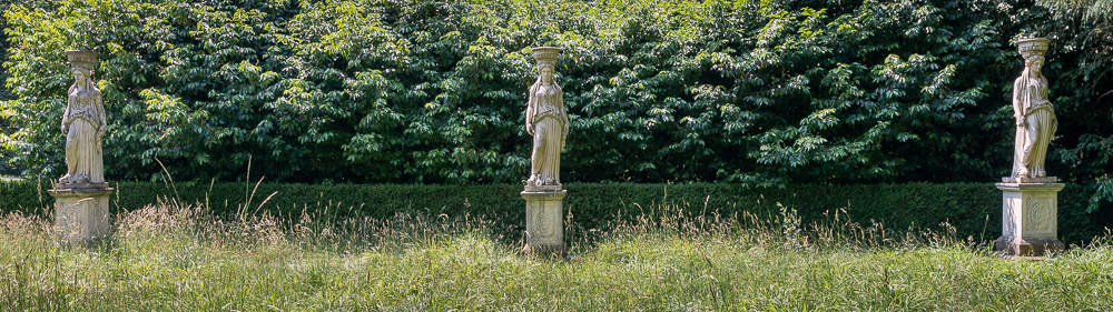 Row of three caryatids in front off a hedge