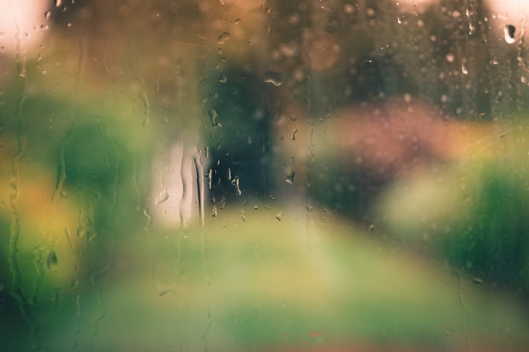 Rain pouring down a window and scene beyond is out of focus with orange glow of sunset